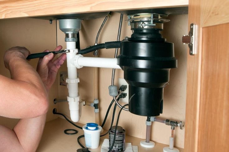 Plumber installing a garbage disposal beneath a kitchen sink in Englewood